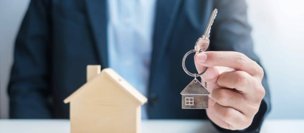 Man holding key with a mini house on a desk