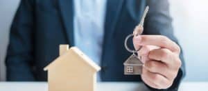 Man holding key with a mini house on a desk