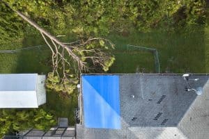 Aerial view of damaged in hurricane Ian house roof covered with blue protective tarp against rain water leaking until replacement of asphalt shingles