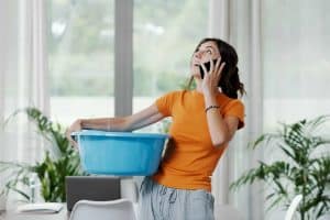 Young upset woman collecting water leaking and dripping from the ceiling, she is calling the roofer