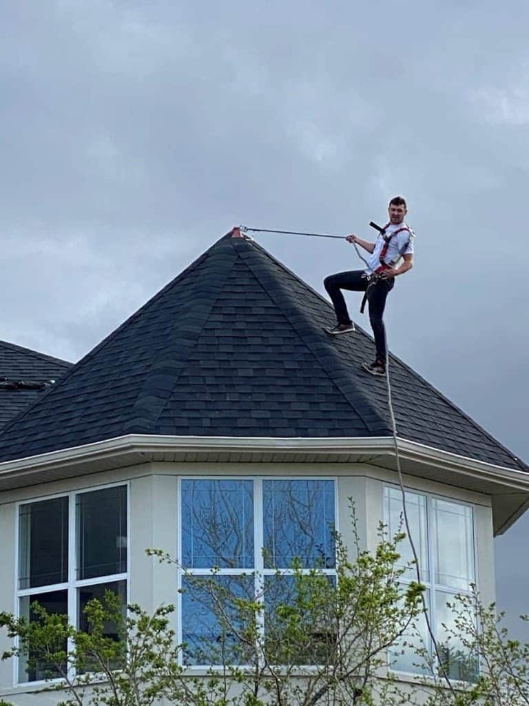 A roofer on top of a steep roof using his safety harness