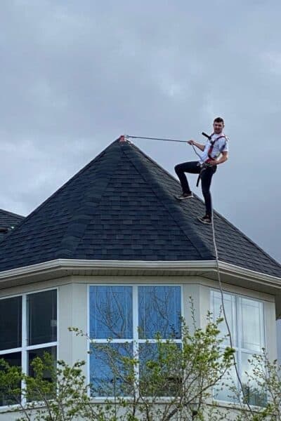 A roofer on top of a steep roof using his safety harness