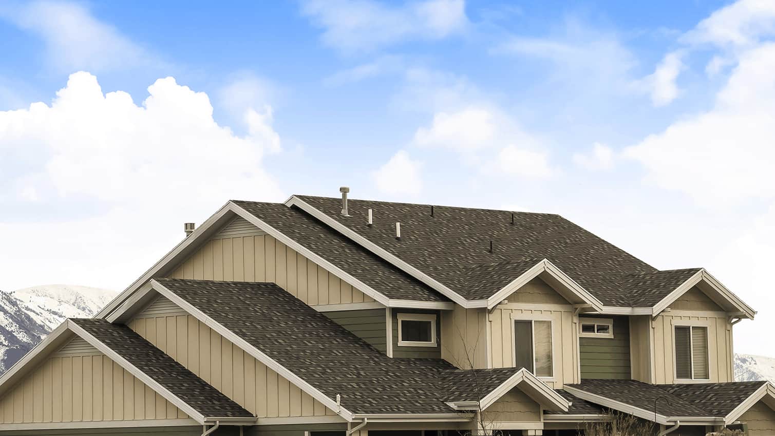 Beautiful residential roof with dark shingles and green siding under a clear blue sky, showcasing quality roofing craftsmanship in Calgary.