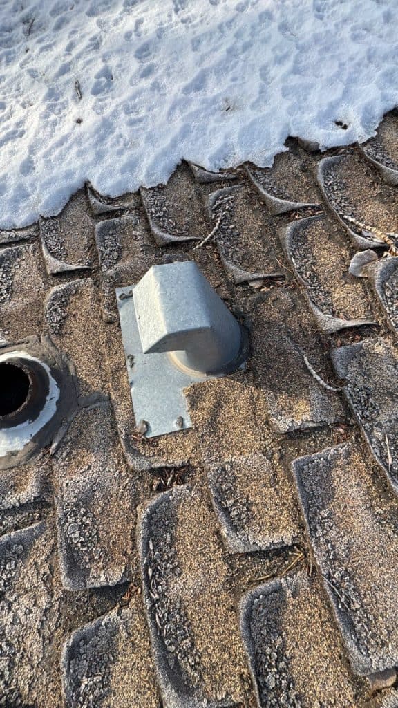 A roof in Calgary in winter showing old cracked shingles next to a roofing vent that needs to be replaced.