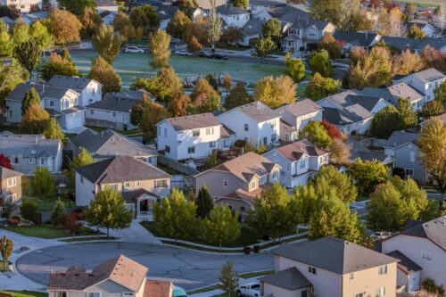 Aerial view of Calgary suburban homes with a mix of roof styles and materials surrounded by autumn trees