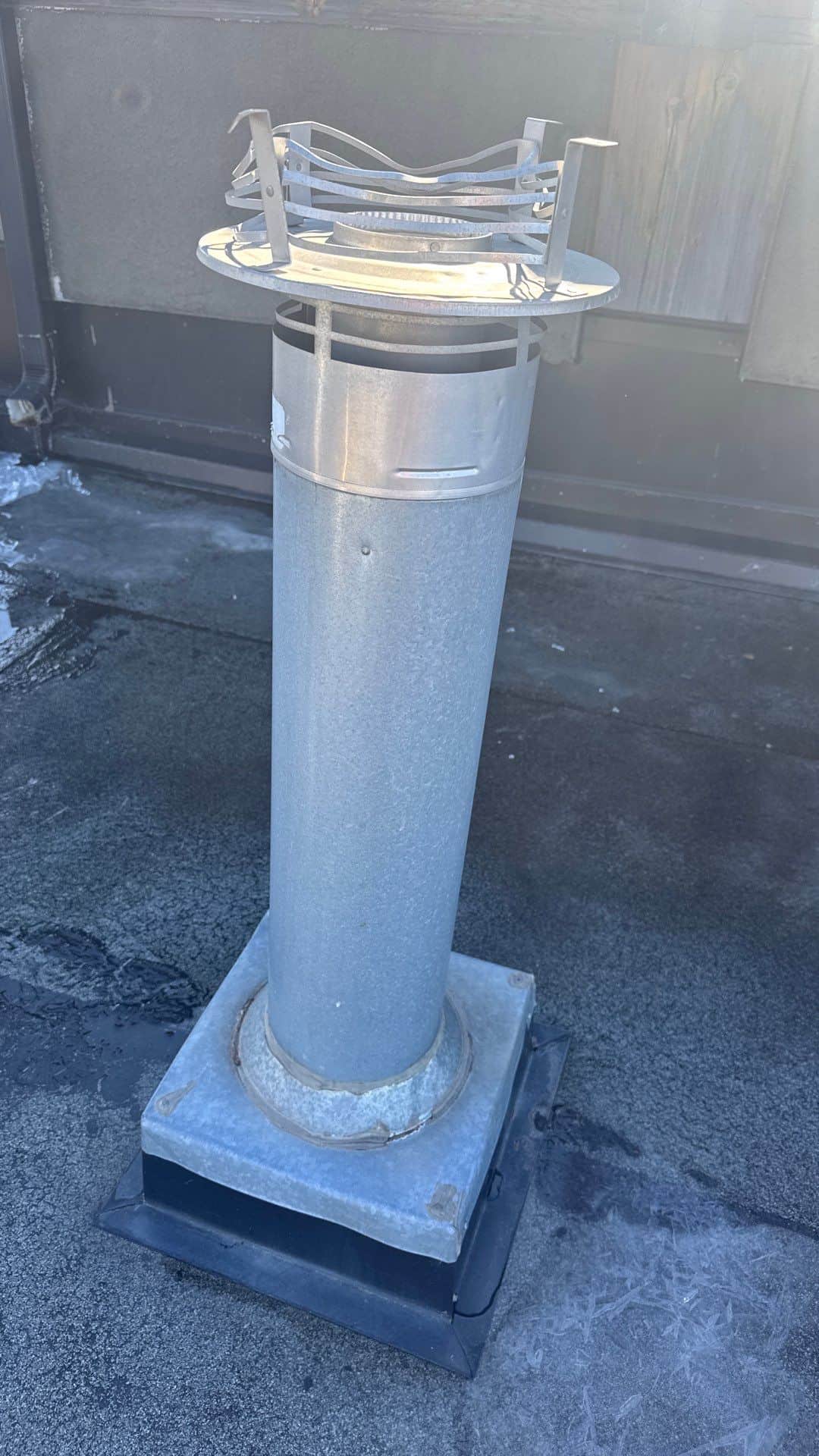 Galvanized furnace cap on a Calgary roof with the upper cage splayed open after high winds, allowing water to enter the flue.